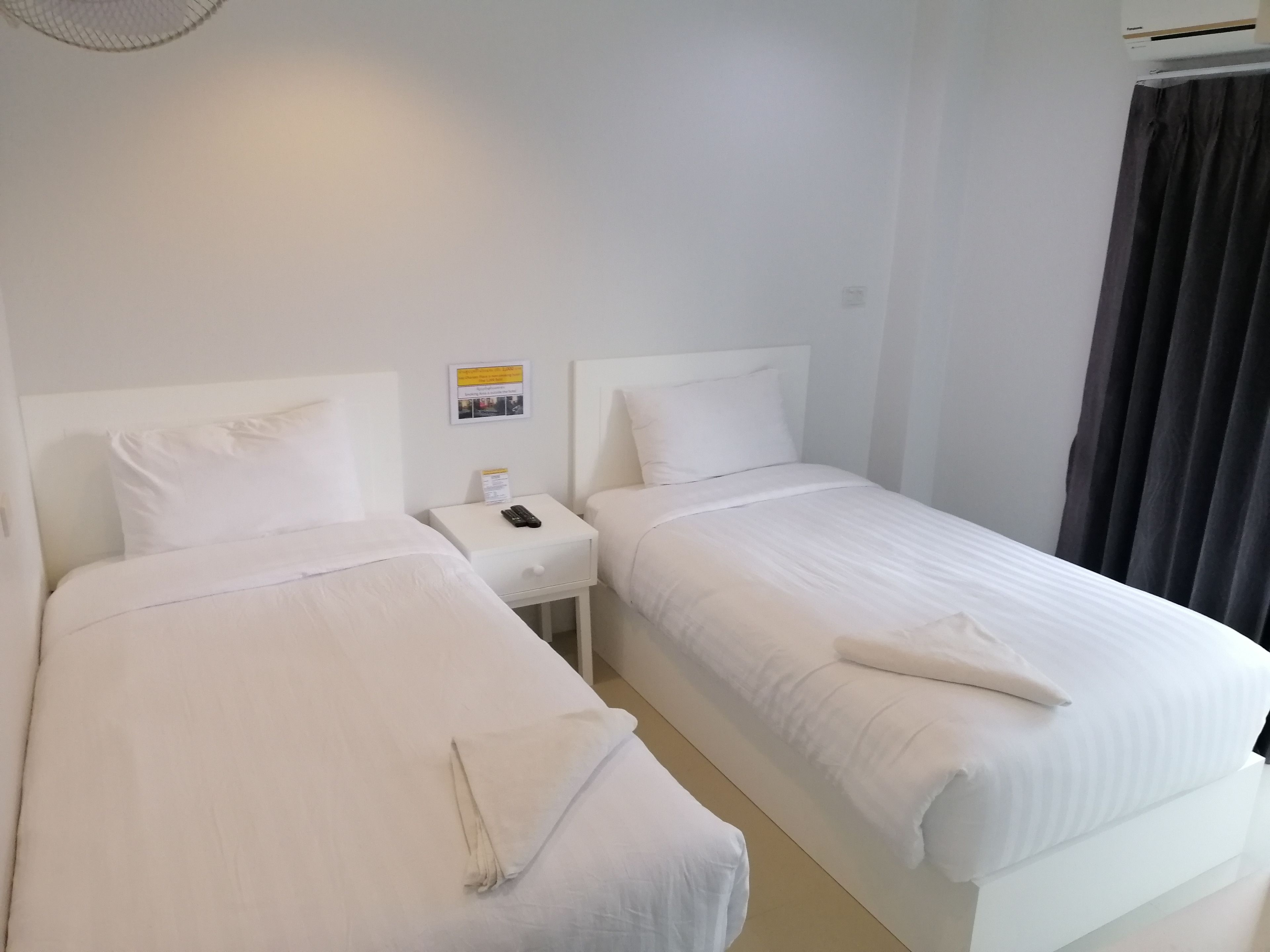 A hotel room with two single beds, a small bedside table with a phone, and a wall-mounted light fixture.