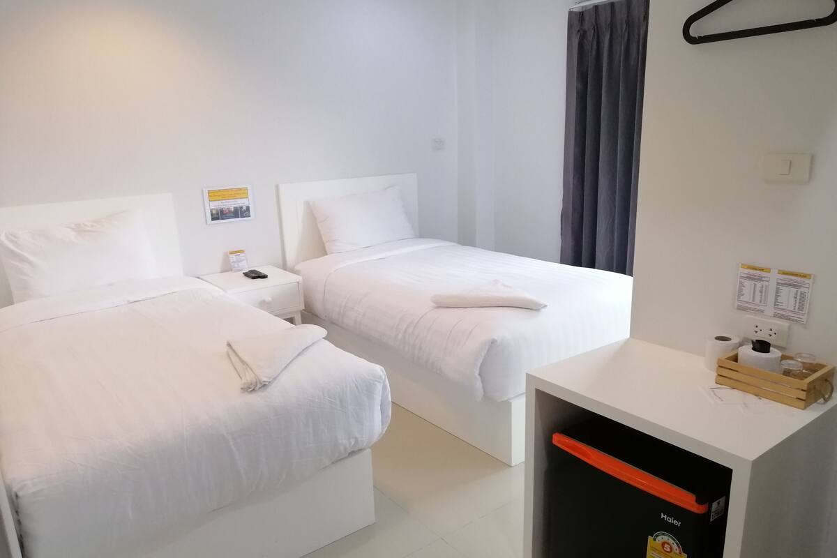 Habitación de hotel con dos camas, un escritorio pequeño con un cesto de basura y un panel informativo en la pared.