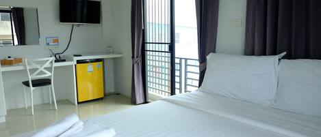 A hotel room with a bed, a desk with a computer, a chair, a TV, and a window with curtains.