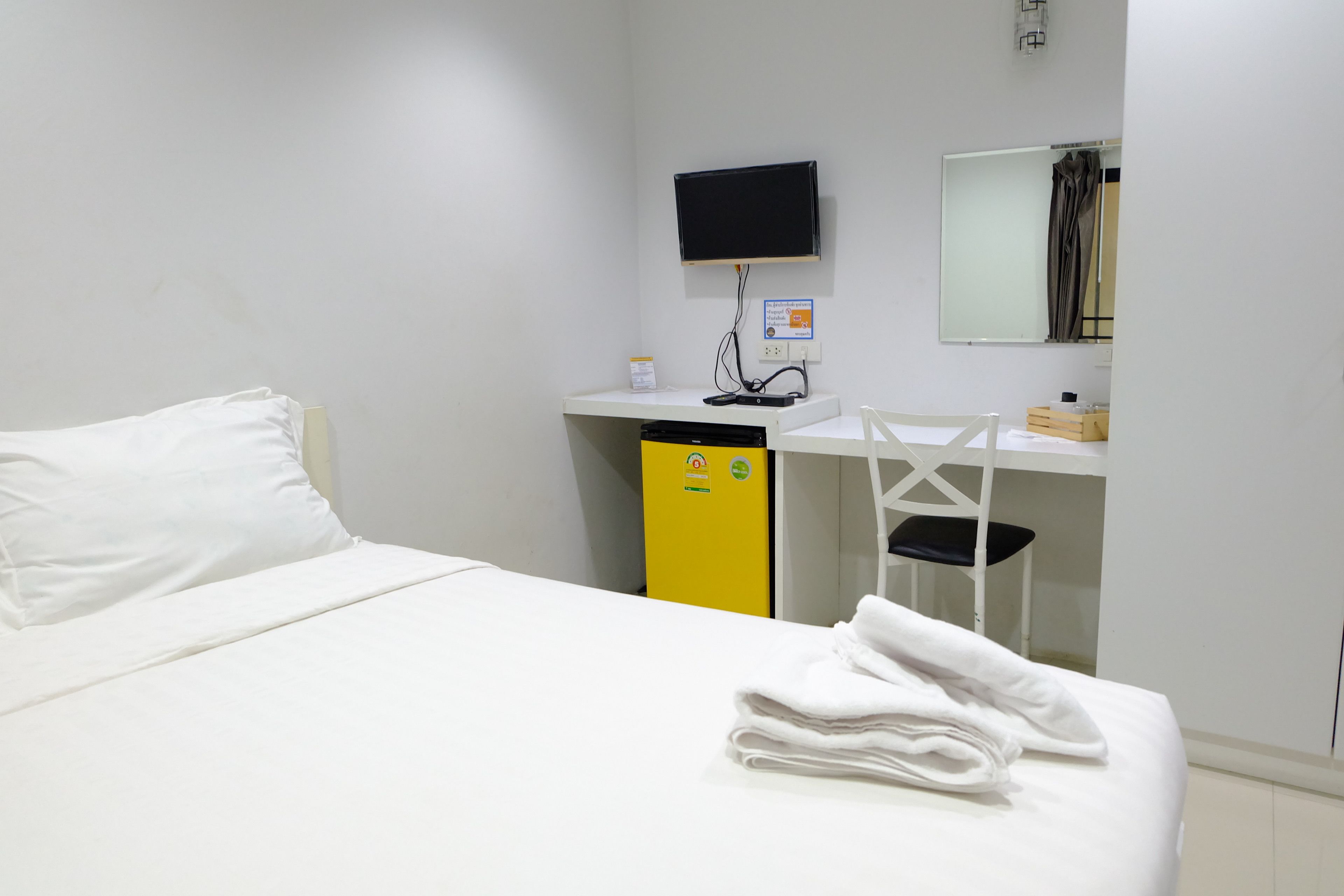 A hotel room with a bed, a desk with a computer, a chair, and a television mounted on the wall.
