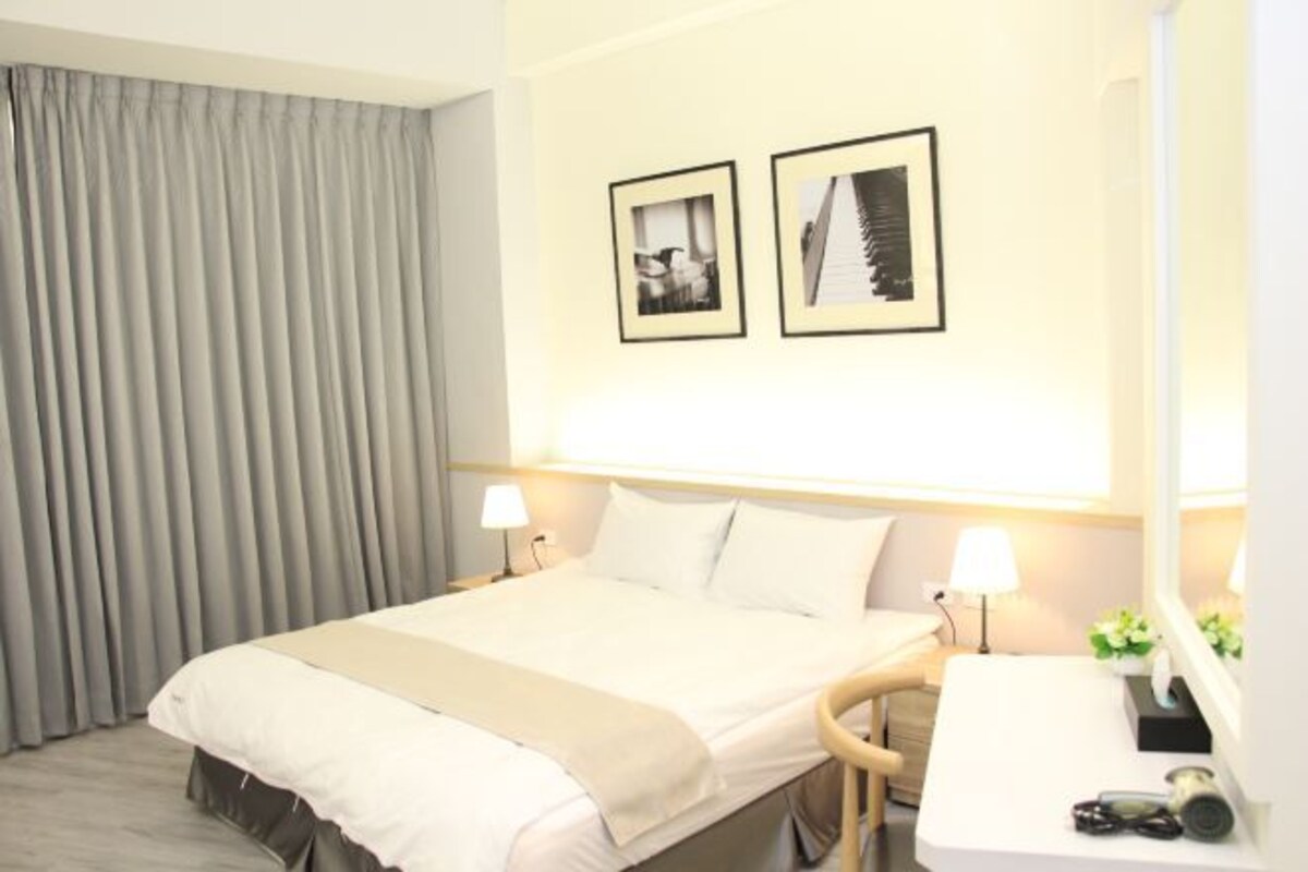 A hotel room with a bed, bedside lamps, a desk with a mirror, and two framed pictures on the wall.