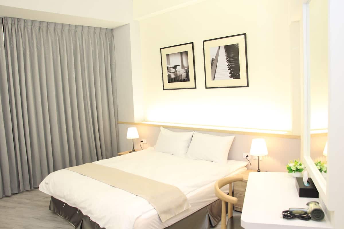 A hotel room with a bed, bedside lamps, a desk with a mirror, and two framed pictures on the wall.