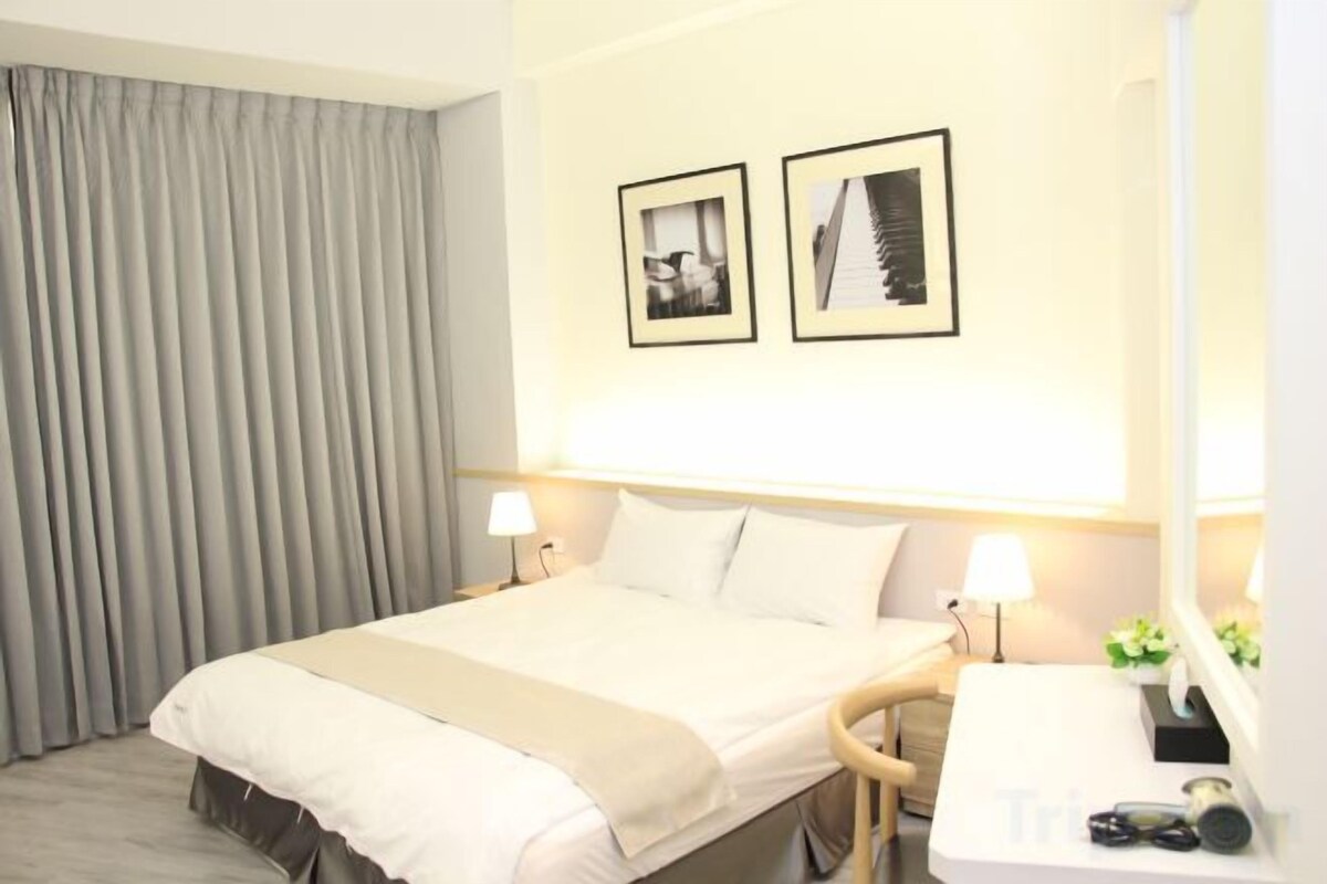 A hotel room with a bed, bedside lamps, a desk with a mirror, and two framed pictures on the wall.