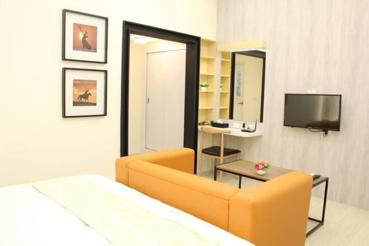 A hotel room with a bed, a desk with a chair, a television, and framed pictures on the wall.