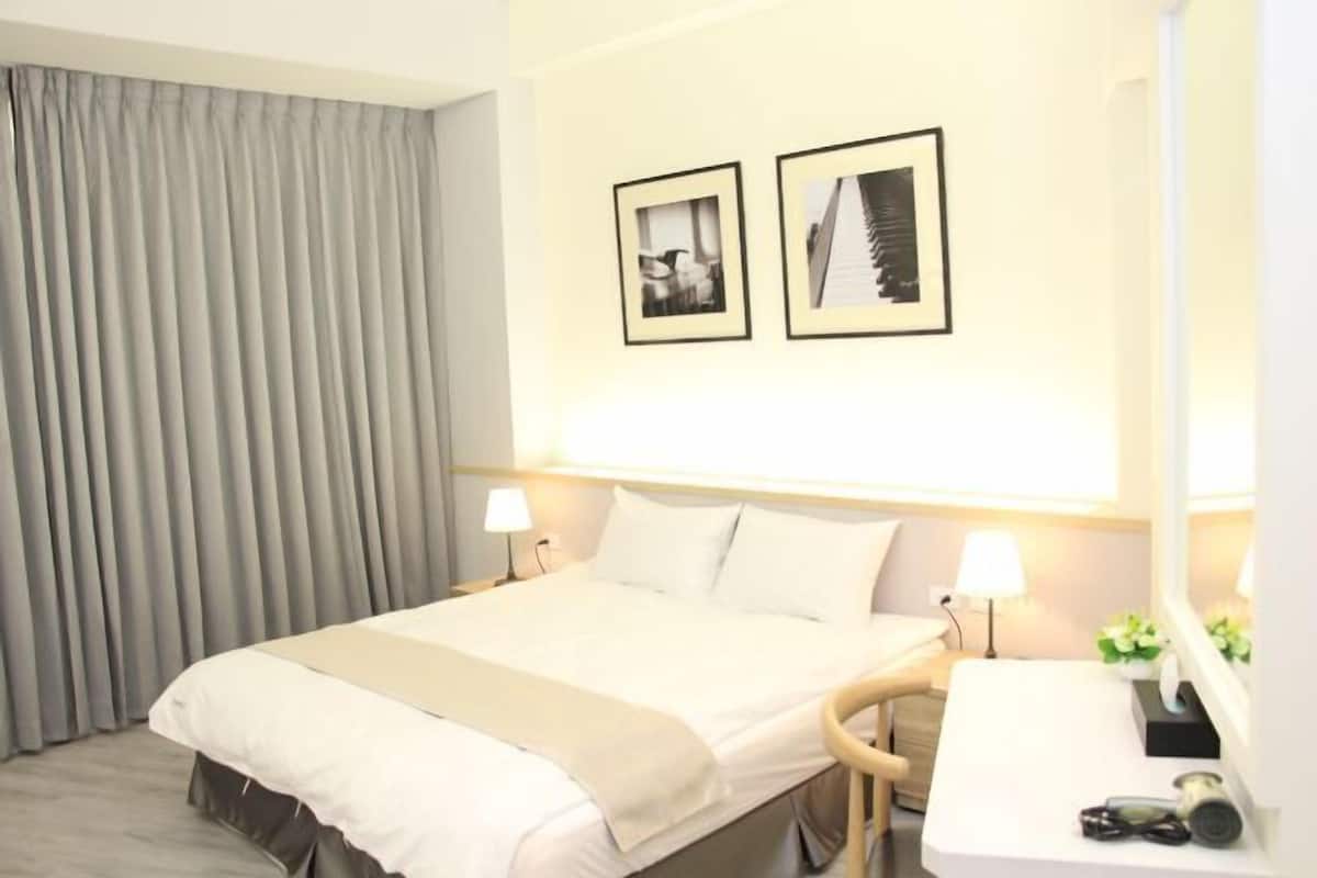 A hotel room with a bed, bedside lamps, a desk with a mirror, and two framed pictures on the wall.
