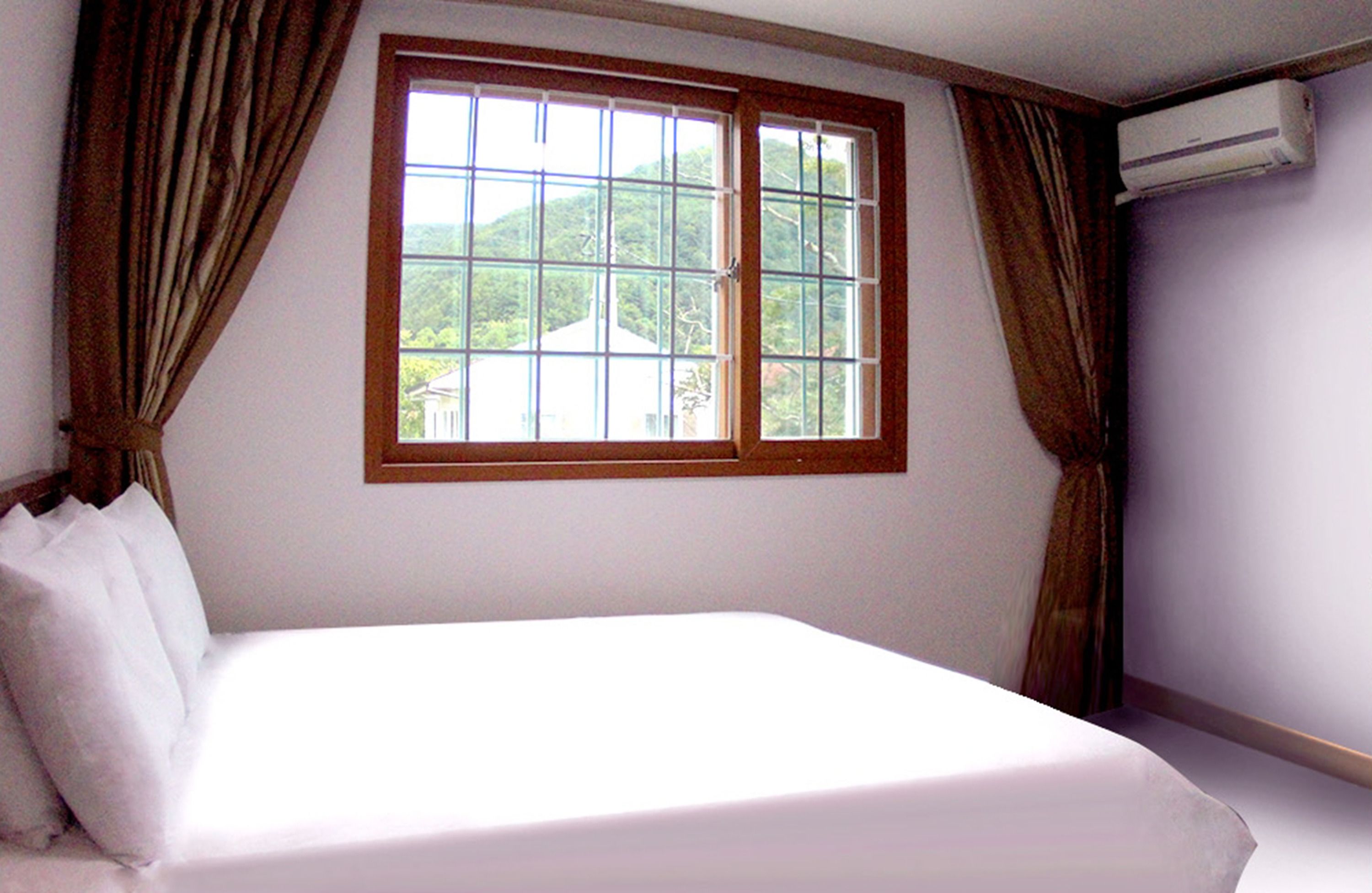 A bedroom with a large window, a bed, and an air conditioning unit.