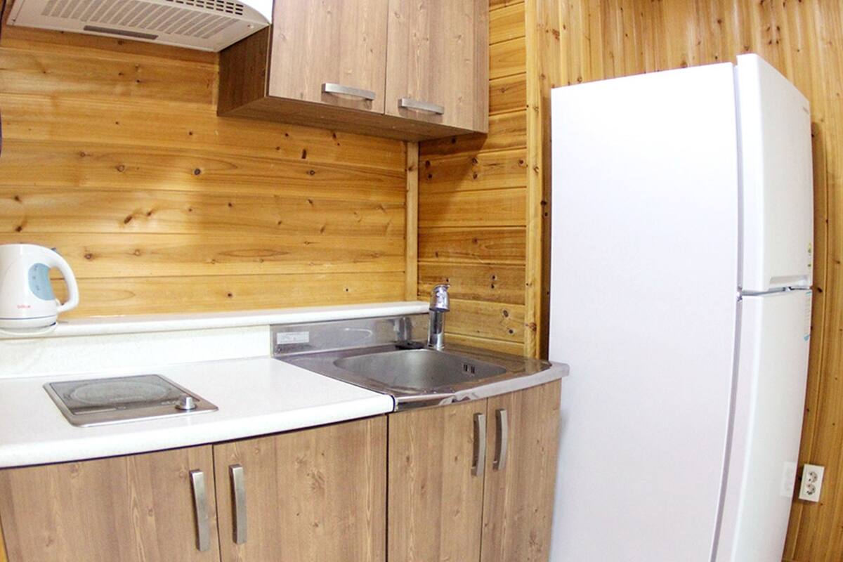 A kitchen with wooden cabinets, a sink, a kettle, and a white refrigerator.