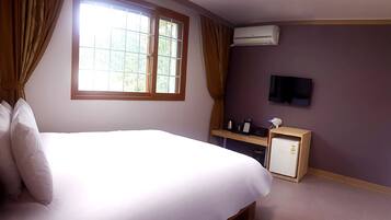 A bedroom with a bed, a window with curtains, a television, and a small refrigerator.
