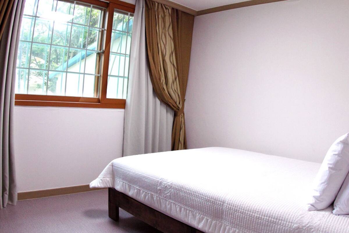 A bedroom with a bed, a window with curtains, and a view of greenery outside.