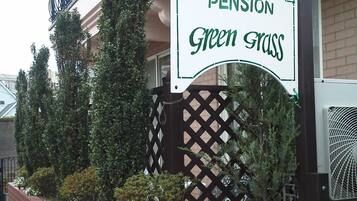 A sign for "Pension Green Grass" with a brick wall and potted plants in front.