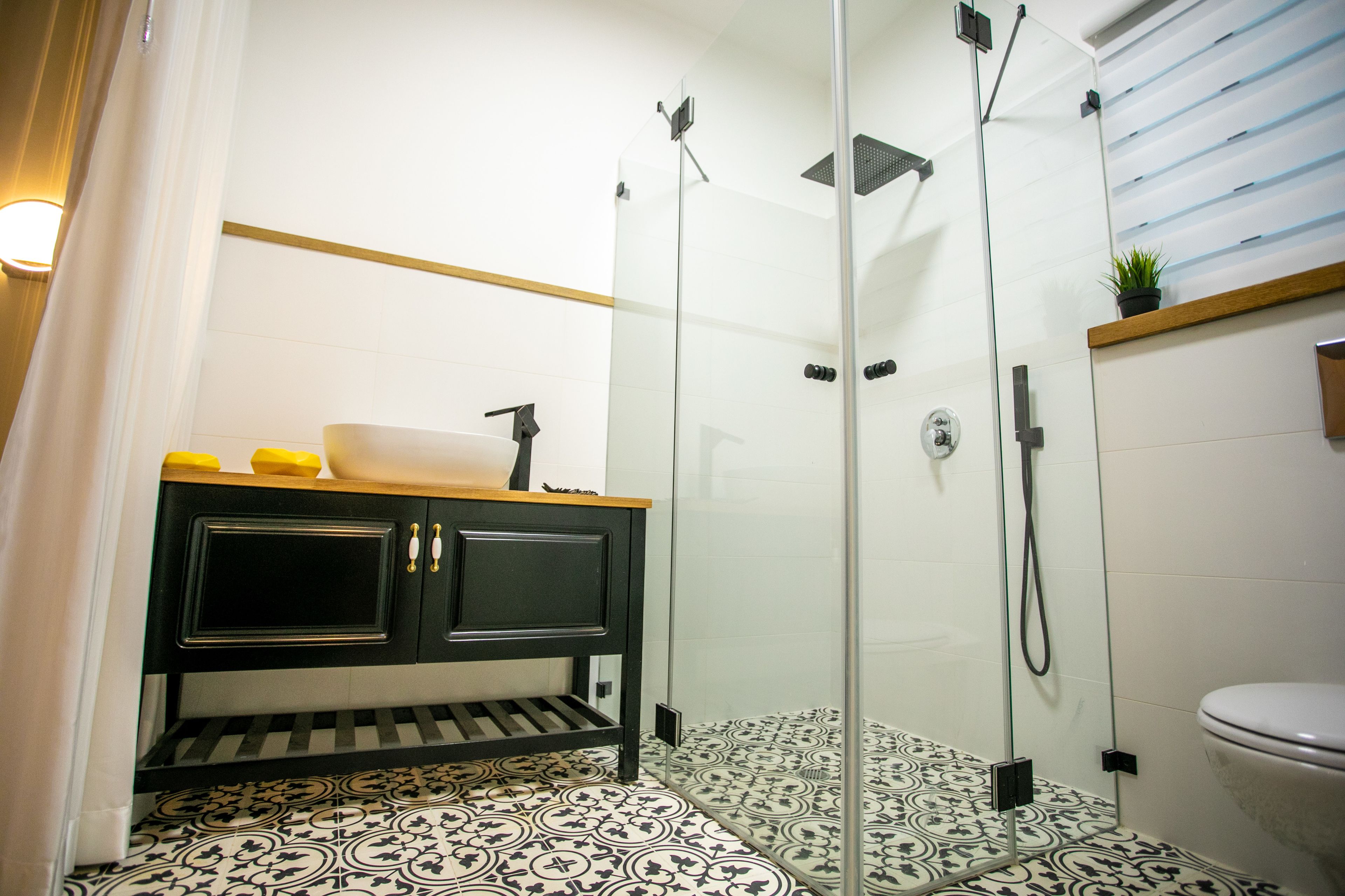 A bathroom with a glass-enclosed shower, a black vanity with a yellow soap dish, and a patterned floor.