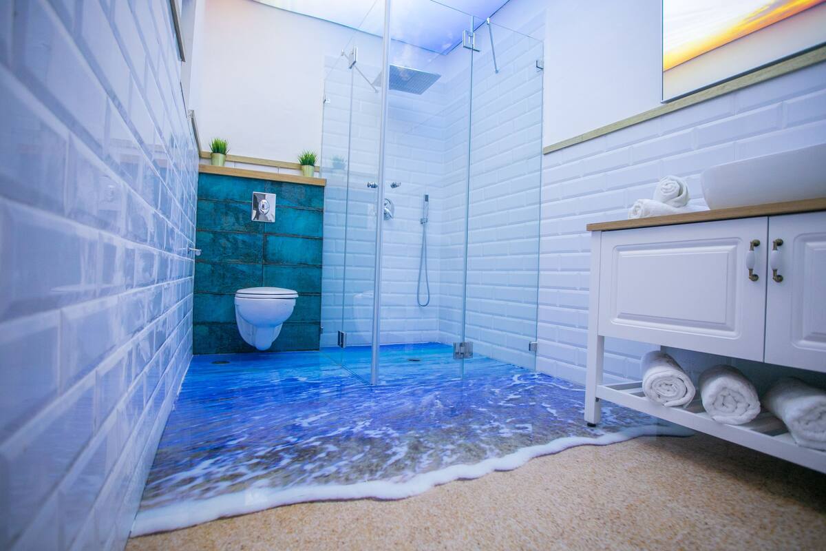 A bathroom with a glass shower enclosure, a white toilet, and a shelf with towels.