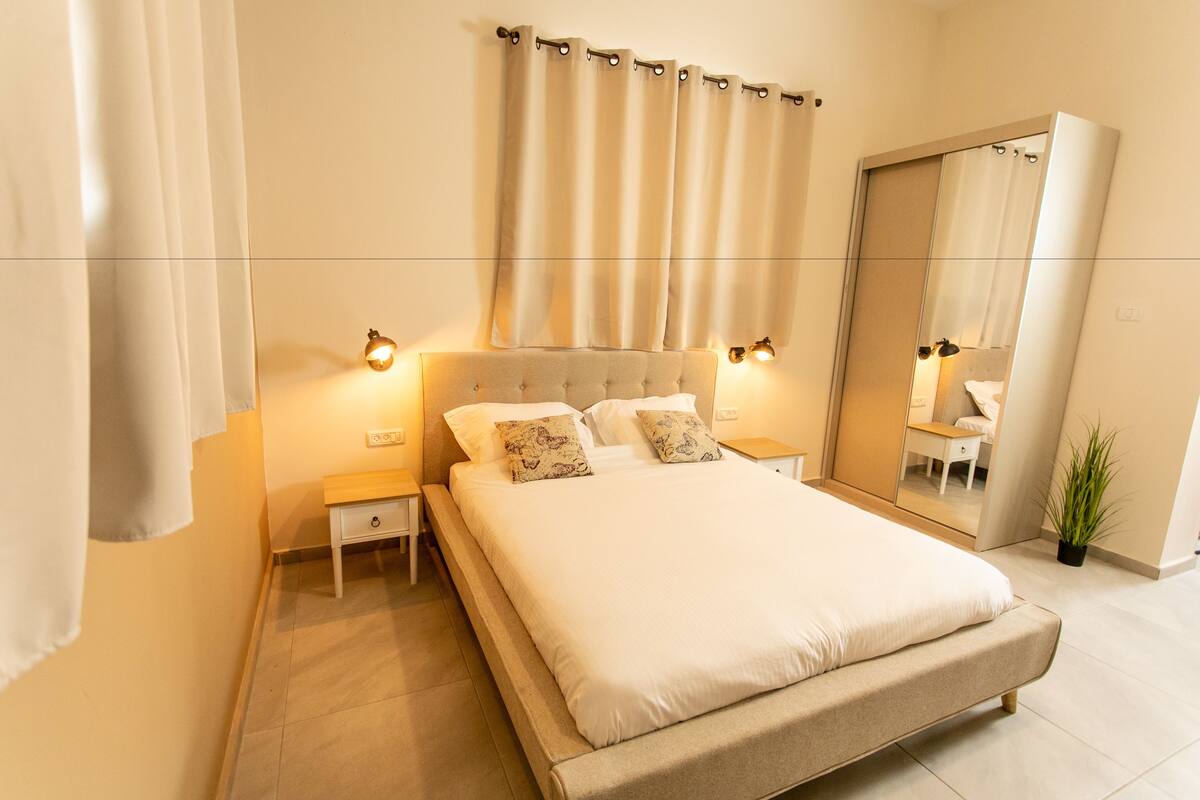 A bedroom with a large bed, bedside tables, a mirror, and a potted plant.