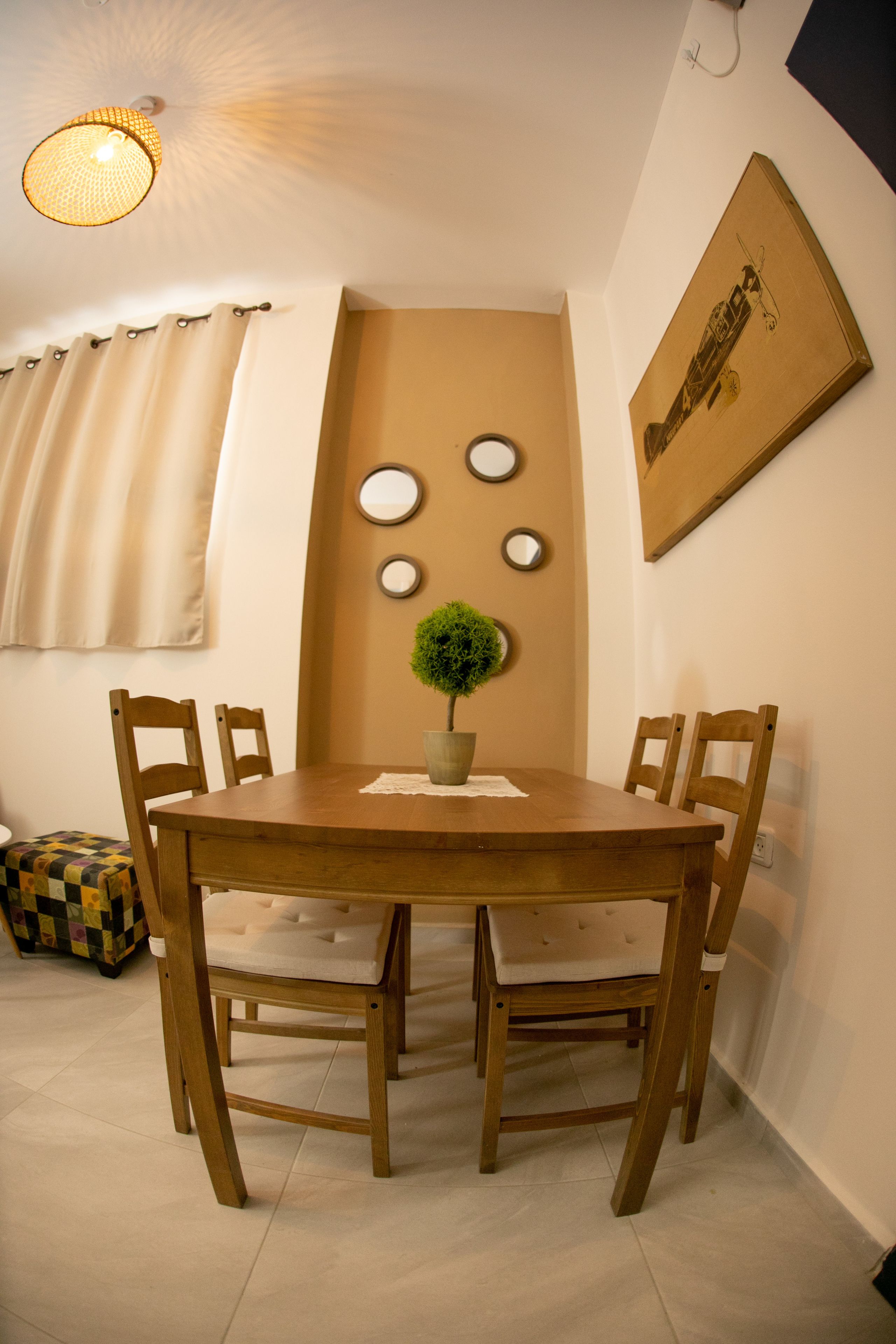 A dining area with a wooden table, four chairs, a potted plant, and a wall-mounted mirror.