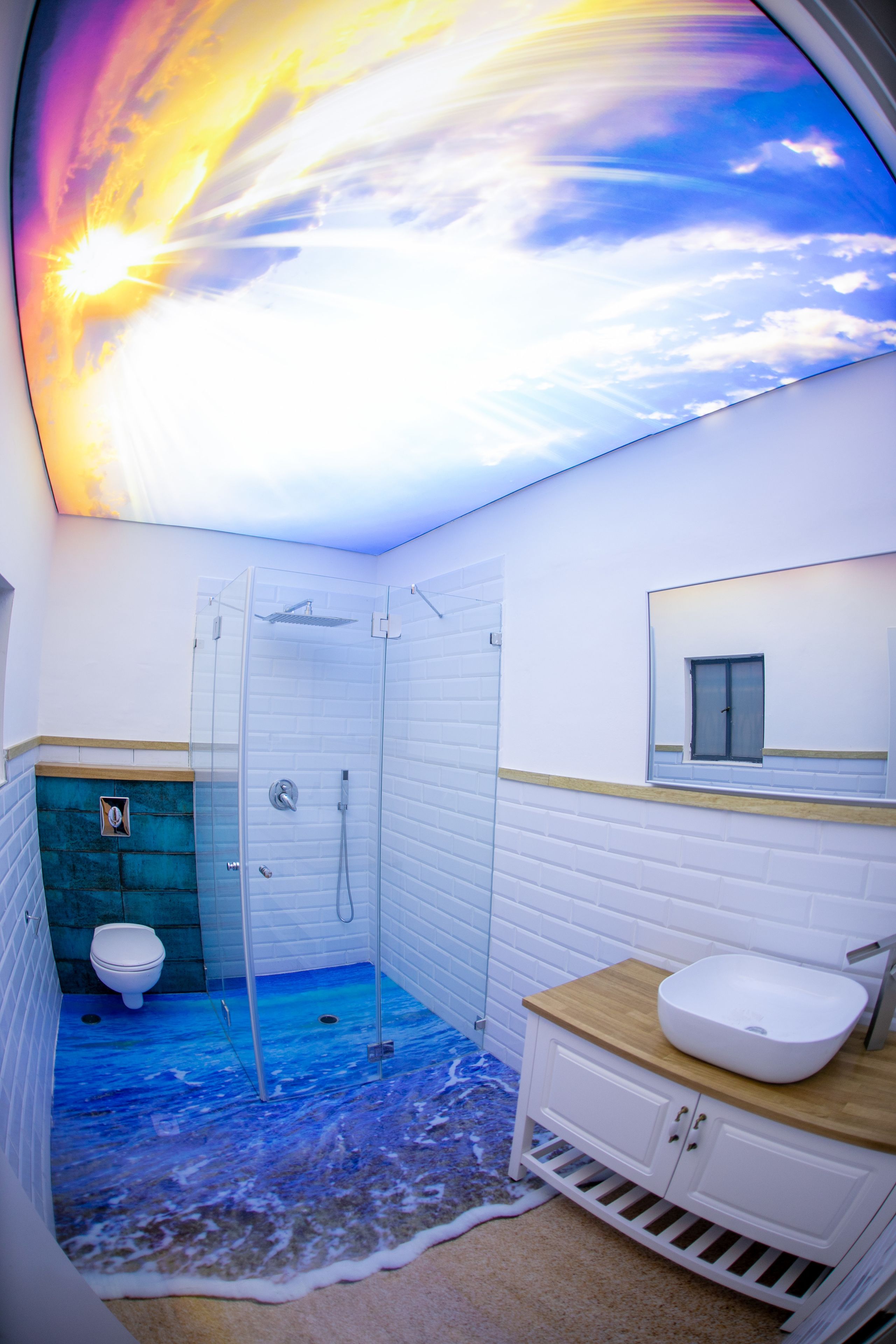 Un bagno con un affresco al soffitto raffigurante un'alba, cabina doccia in vetro, un water bianco e un mobile bagno in legno con lavabo.