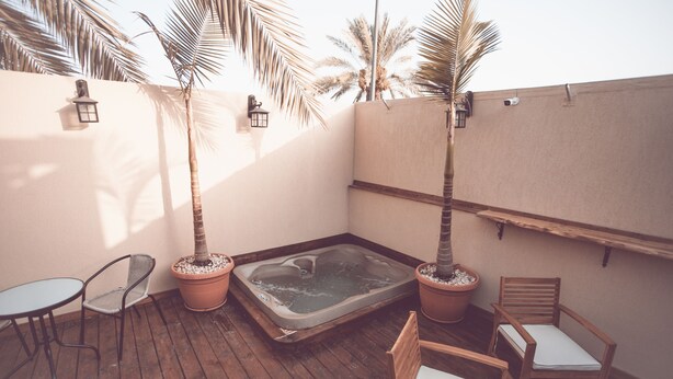 Terraza de madera con jacuzzi, dos sillas y palmeras en macetas.