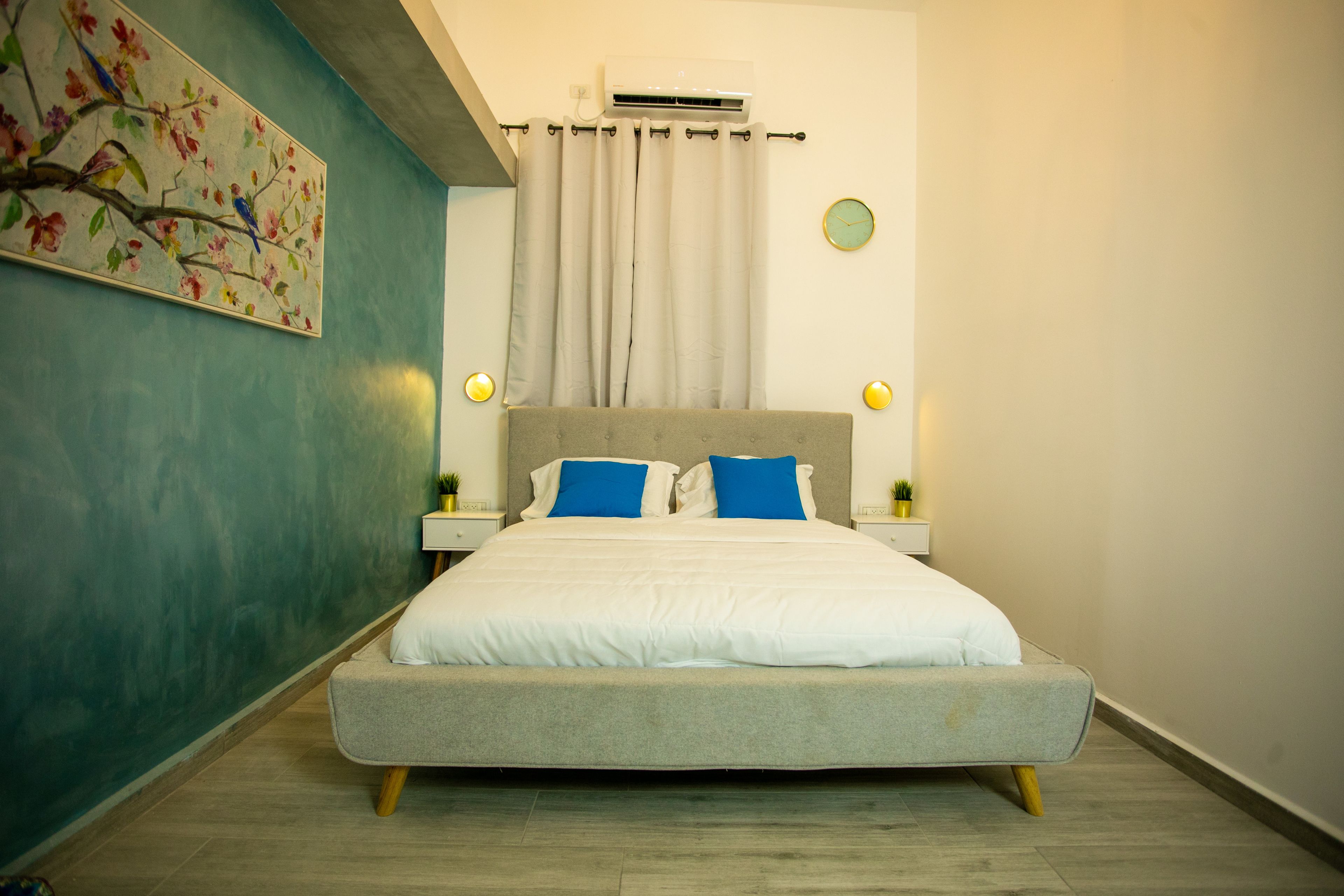 A modern bedroom with a bed, curtains, a wall clock, and a painting.