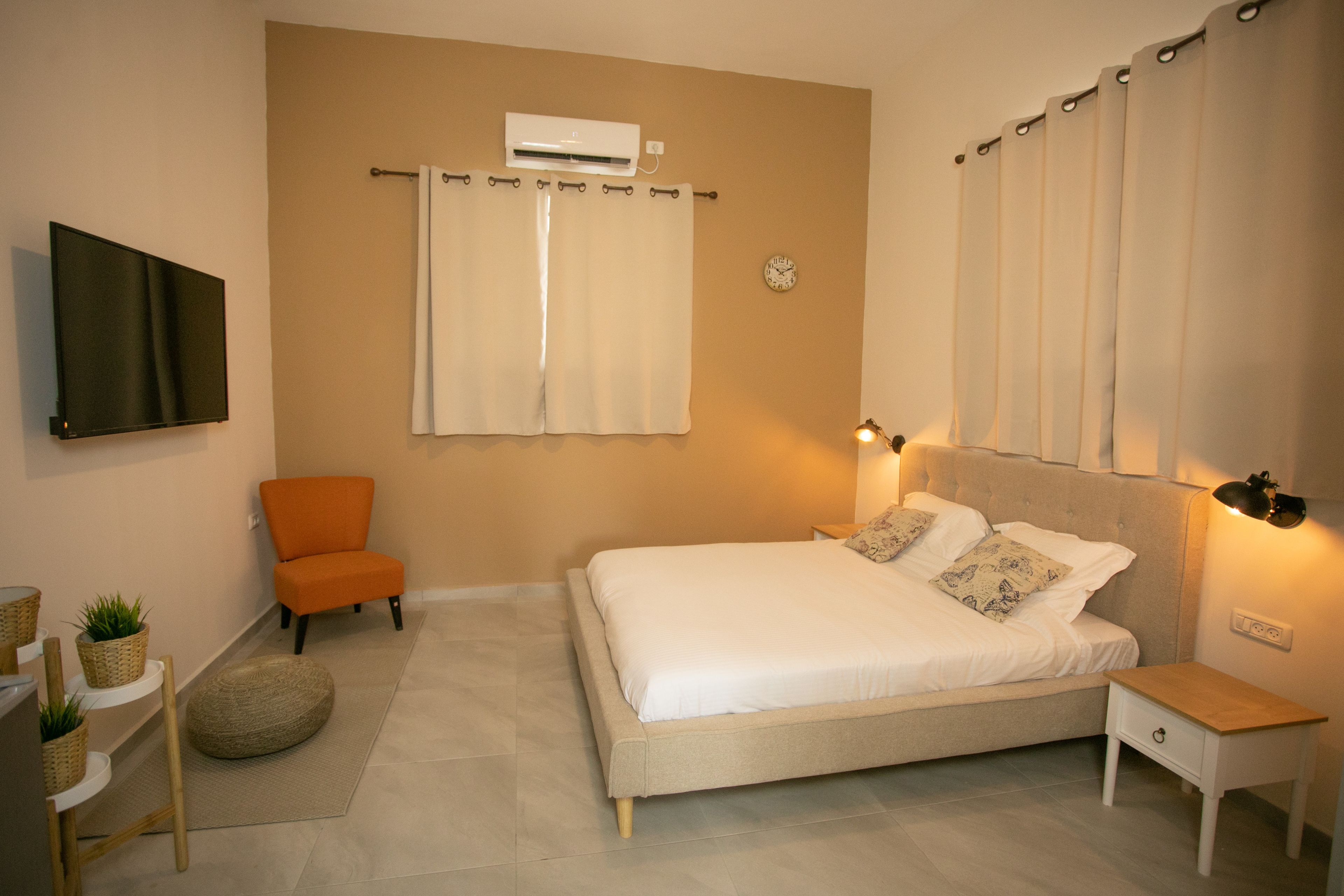 A bedroom with a bed, a chair, a bedside table, an air conditioner, and a wall-mounted TV.