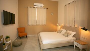 A bedroom with a bed, a chair, a bedside table, an air conditioner, and a wall-mounted TV.
