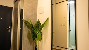 Un interior moderno con suelo de madera, una planta en maceta, un espejo grande y una puerta que da al baño.