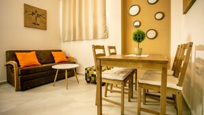 Una sala de estar con un sofá marrón, cojines naranjas, una mesa de comedor de madera con sillas, una mesita redonda y una planta en maceta.