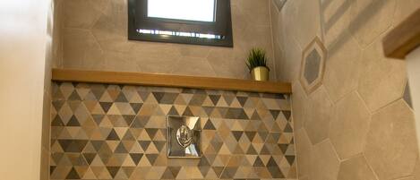Un baño con inodoro, espejo y pared con diseño geométrico.
