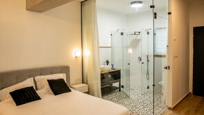 Un dormitorio moderno con una cama grande, cabina de ducha con vidrio y suelo de madera.