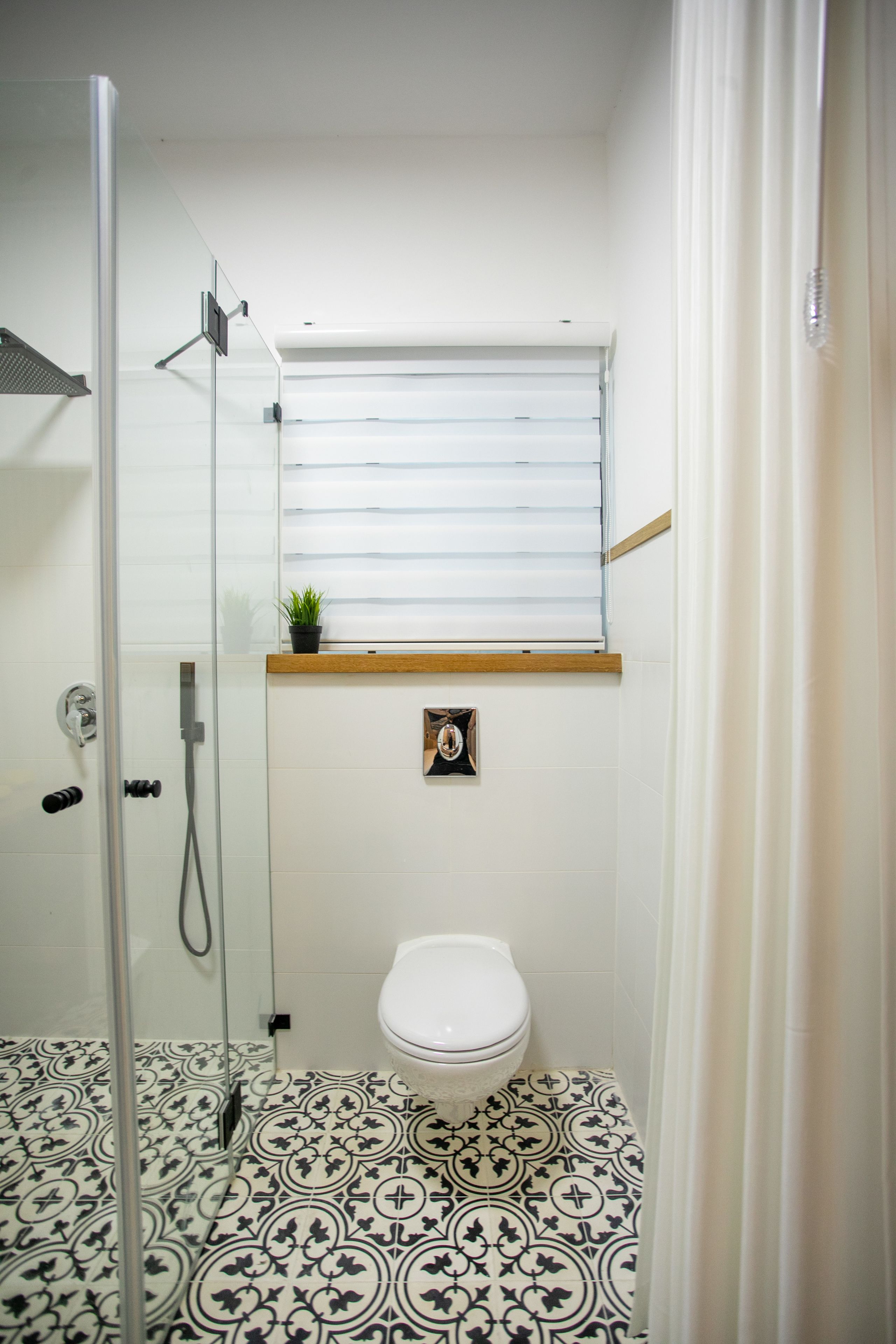 A bathroom with a shower, toilet, and a window with blinds.