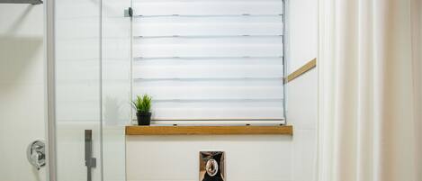 A bathroom with a shower, toilet, and a window with blinds.