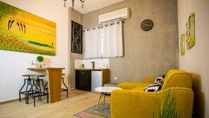 Una sala de estar moderna con un sofá amarillo, una mesita redonda y una cocina con encimera y armarios blancos.