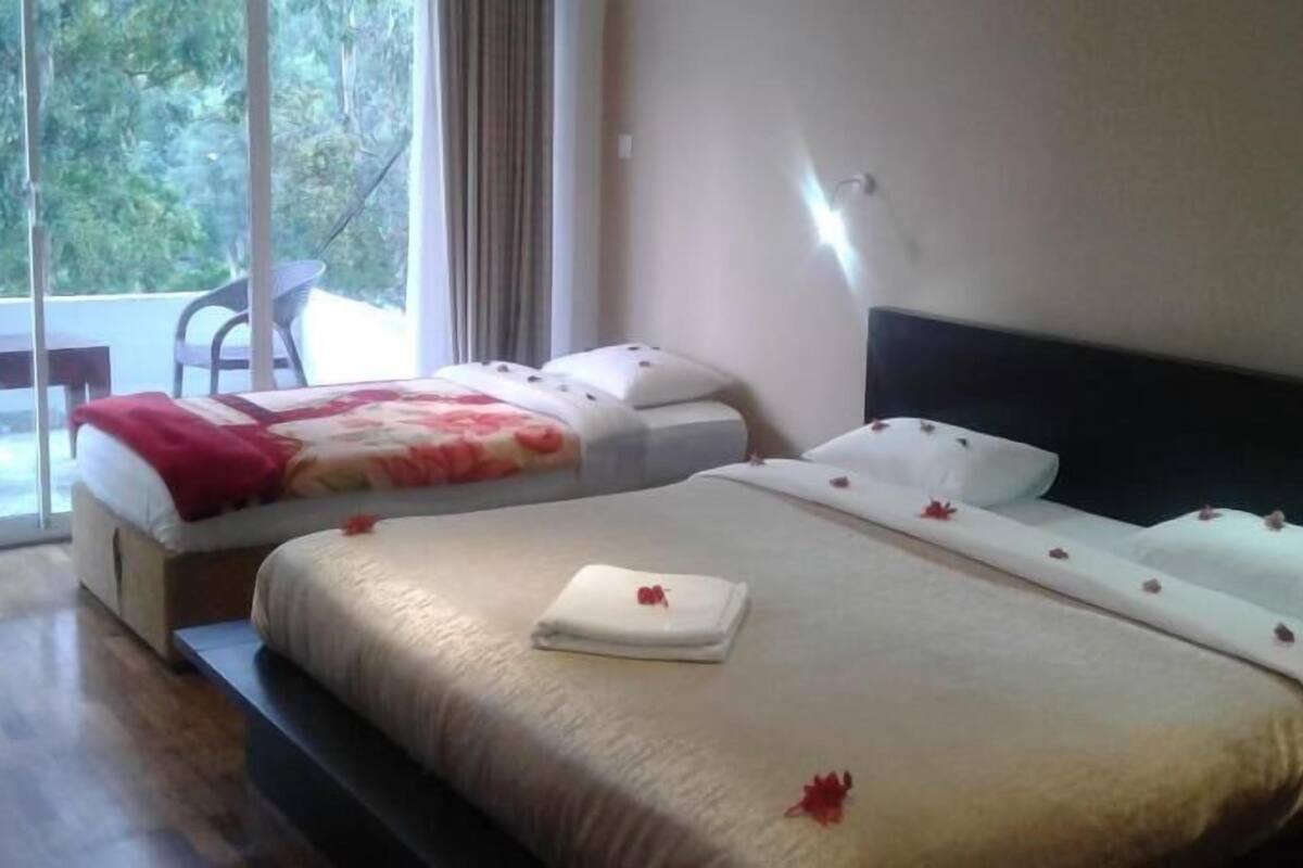 A hotel room with two beds, a large window, and a view of greenery outside.