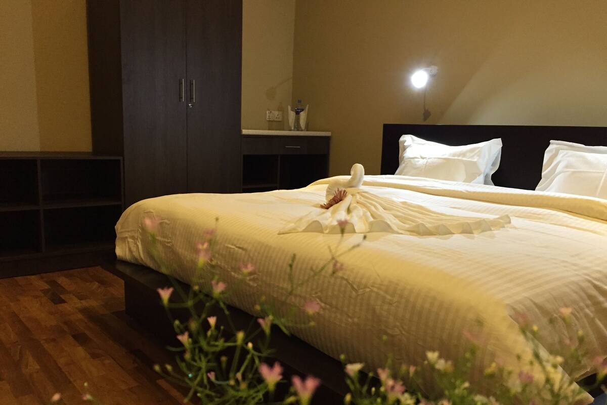 A neatly made bed with a swan decoration, a bedside table with a bottle, and a dark wardrobe in a hotel room.