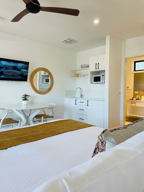Ein modernes Schlafzimmer mit Bett, Schreibtisch, Stuhl, Deckenventilator, Fernseher und einer Küchenzeile mit Schränken und einer Mikrowelle.
