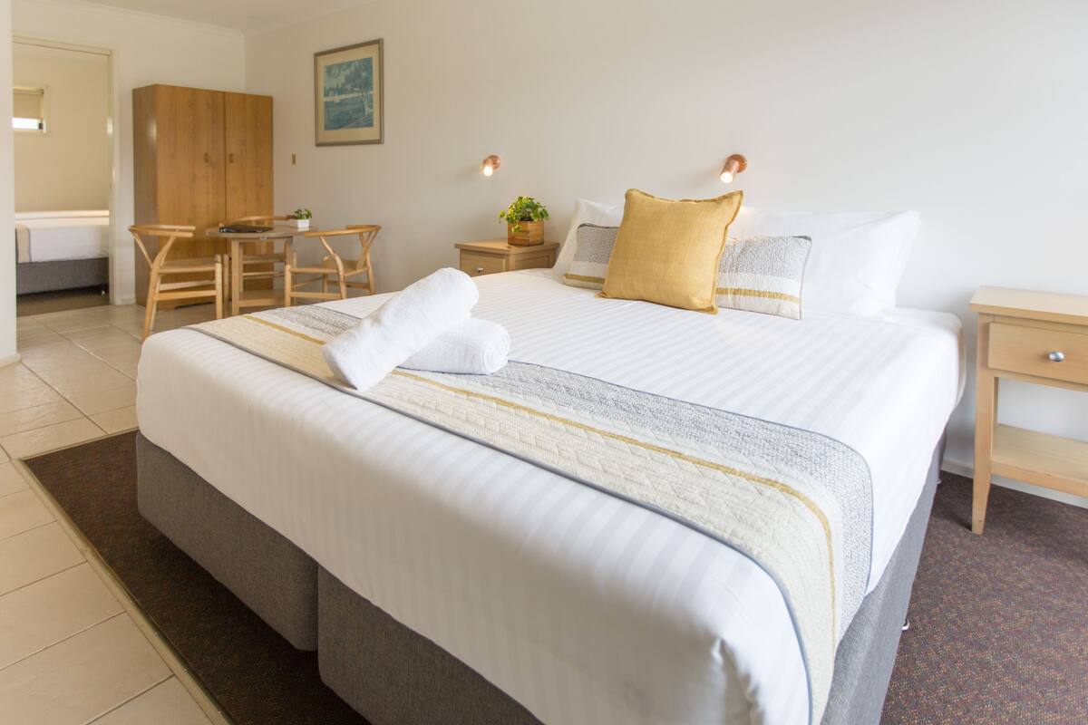 A neatly arranged hotel room with a large bed, a desk, a chair, and a wardrobe.