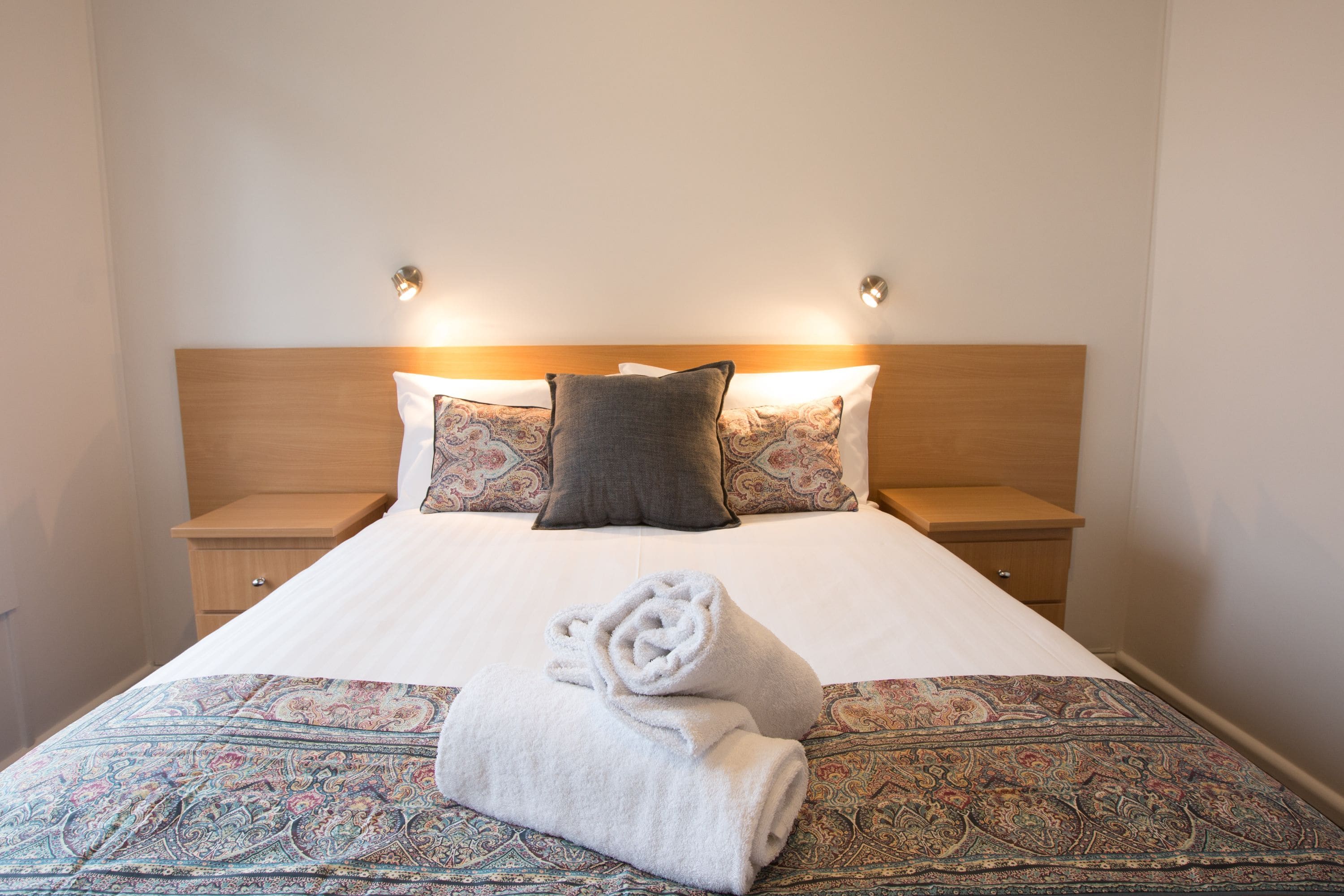 A neatly made bed with patterned bedding, two bedside tables, and wall-mounted lights.
