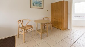 Een kamer met een ronde tafel, twee stoelen, een houten garderobe en een lijst met een afbeelding aan de muur.