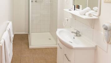 A bathroom with a glass shower enclosure, a sink, and a mirror.