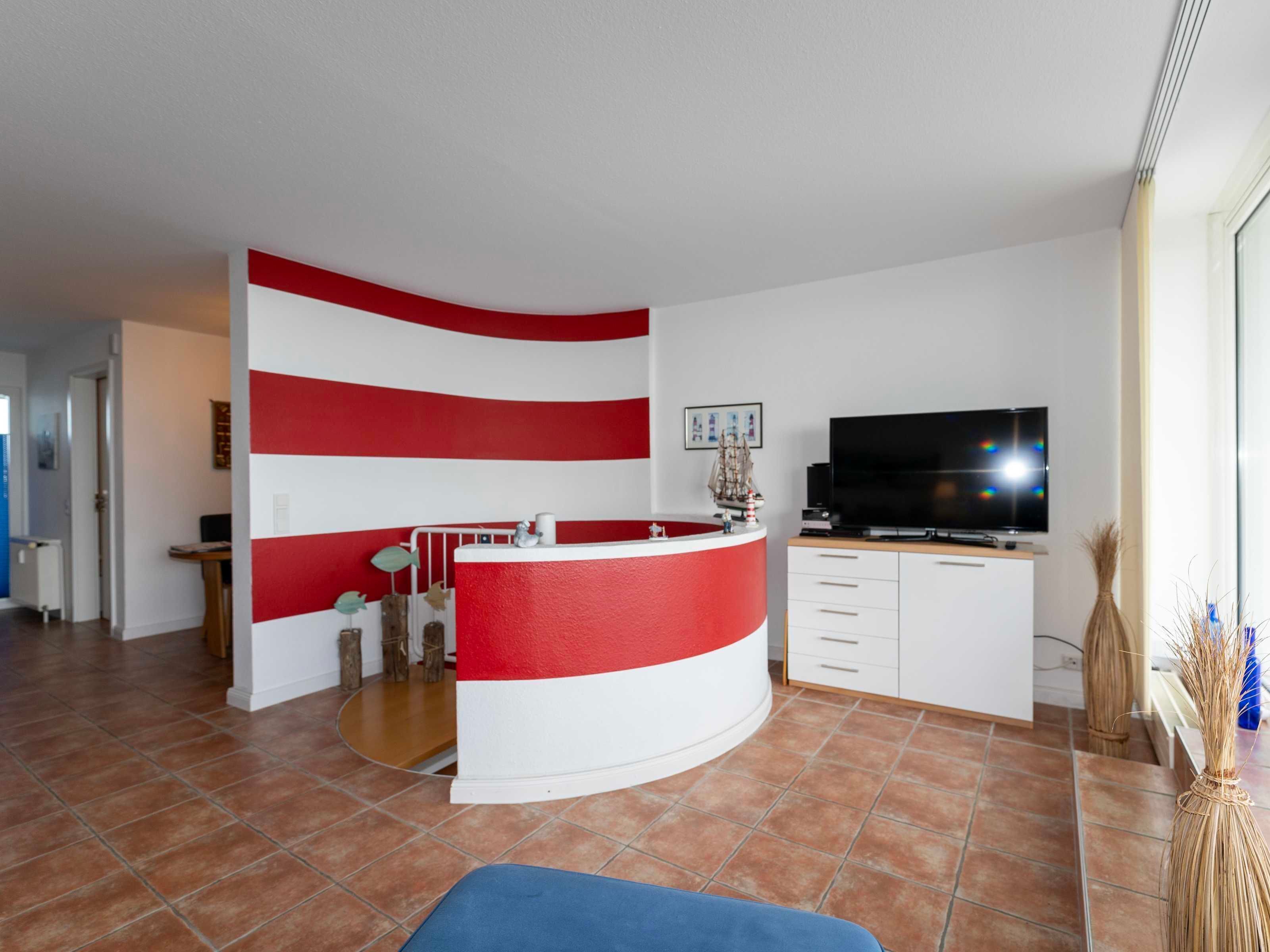 A modern living room with a curved white and red accent wall, a flat-screen TV, and a small dining area.
