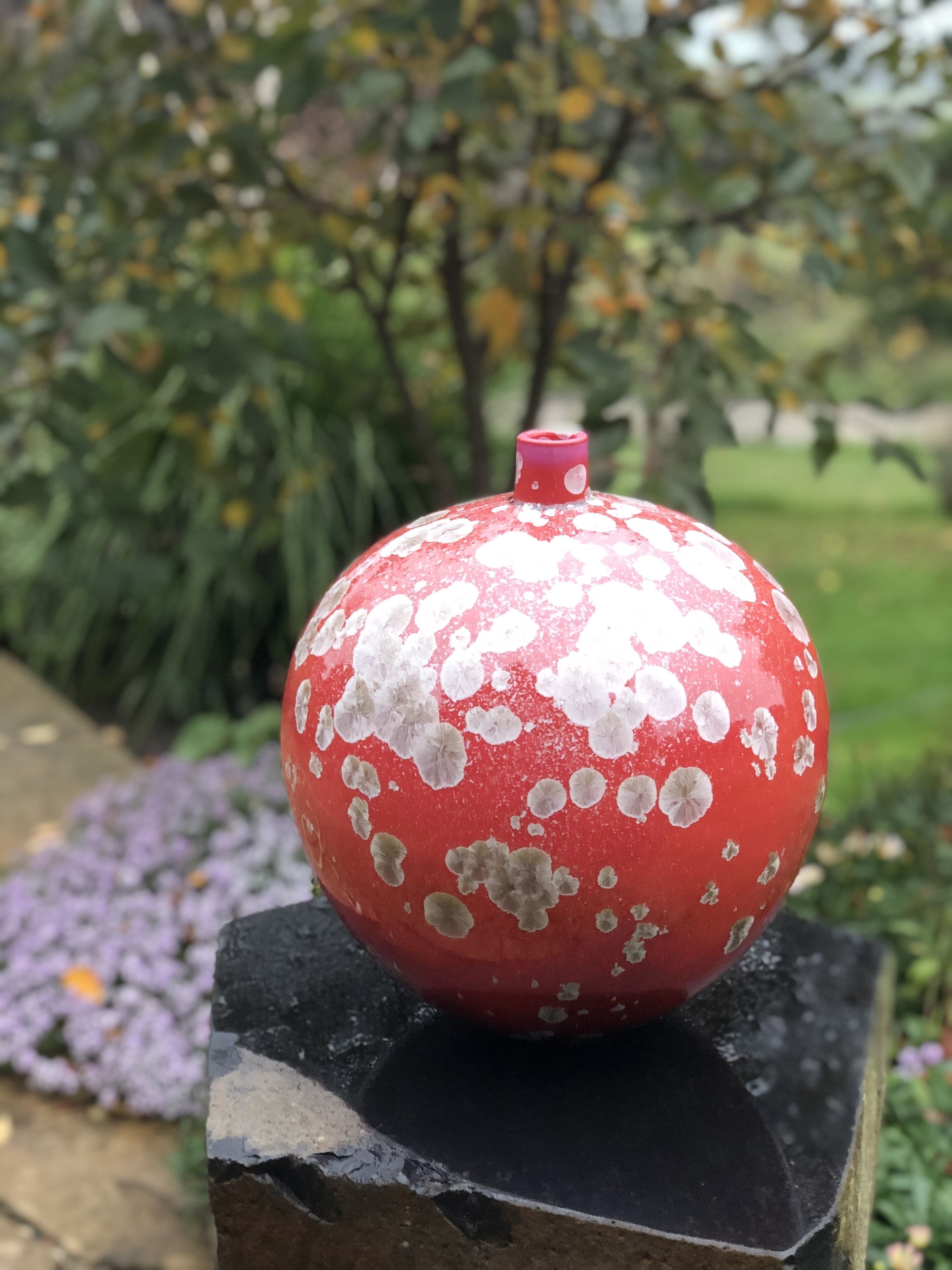 Una granada roja sobre un pedestal de piedra, con un jardín al fondo.