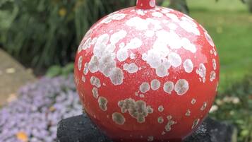Una granada roja sobre un pedestal de piedra, con un jardín al fondo.