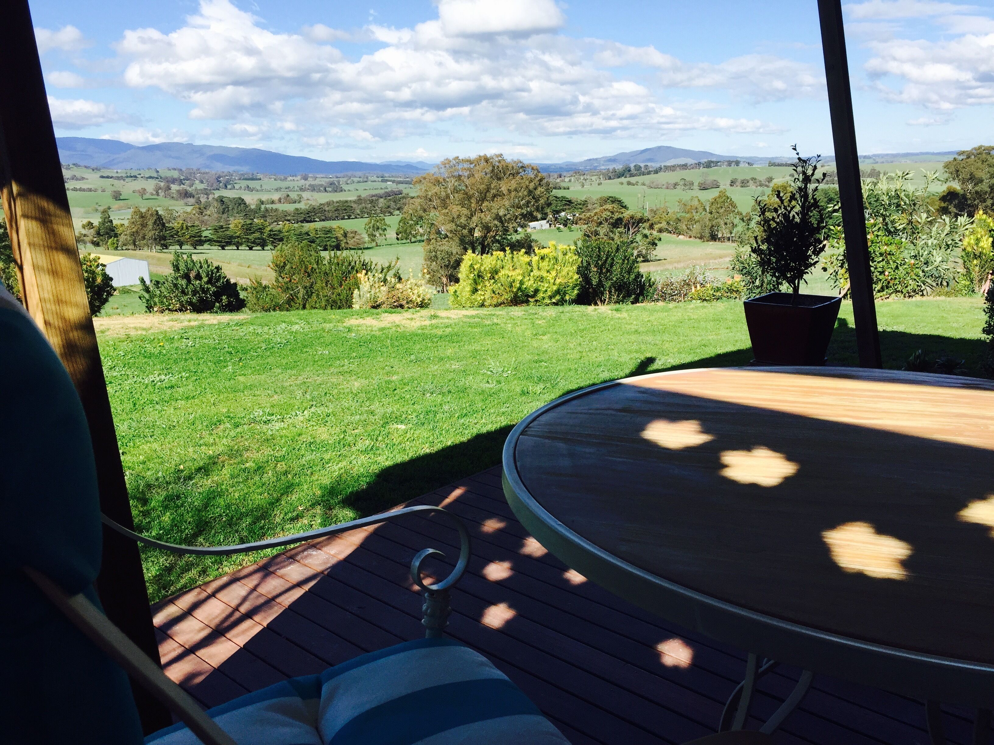 A deck with a view of a grassy field and distant hills.