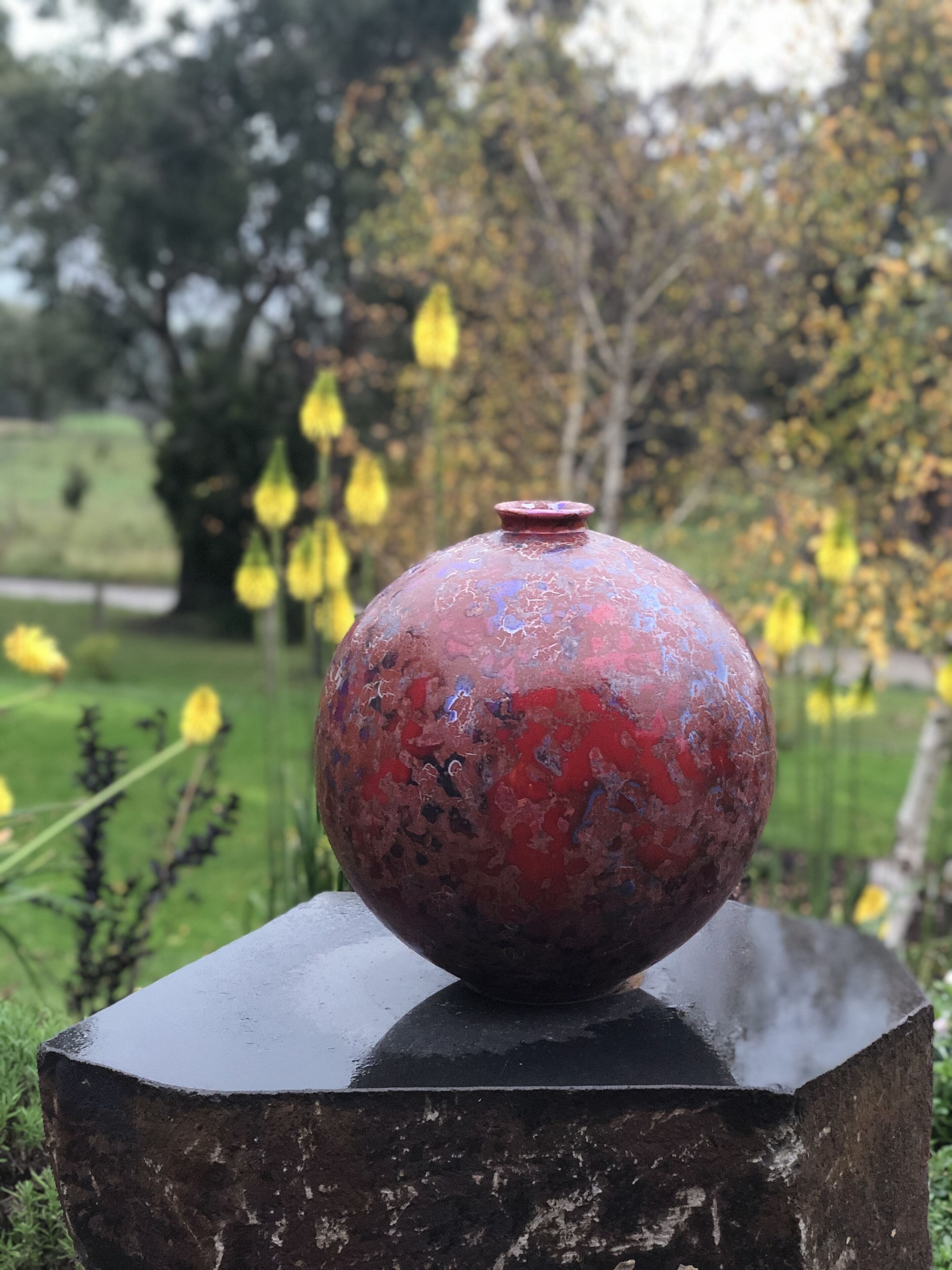 A red vase with a textured surface on a dark, rectangular pedestal.