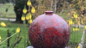 A red vase with a textured surface on a dark, rectangular pedestal.