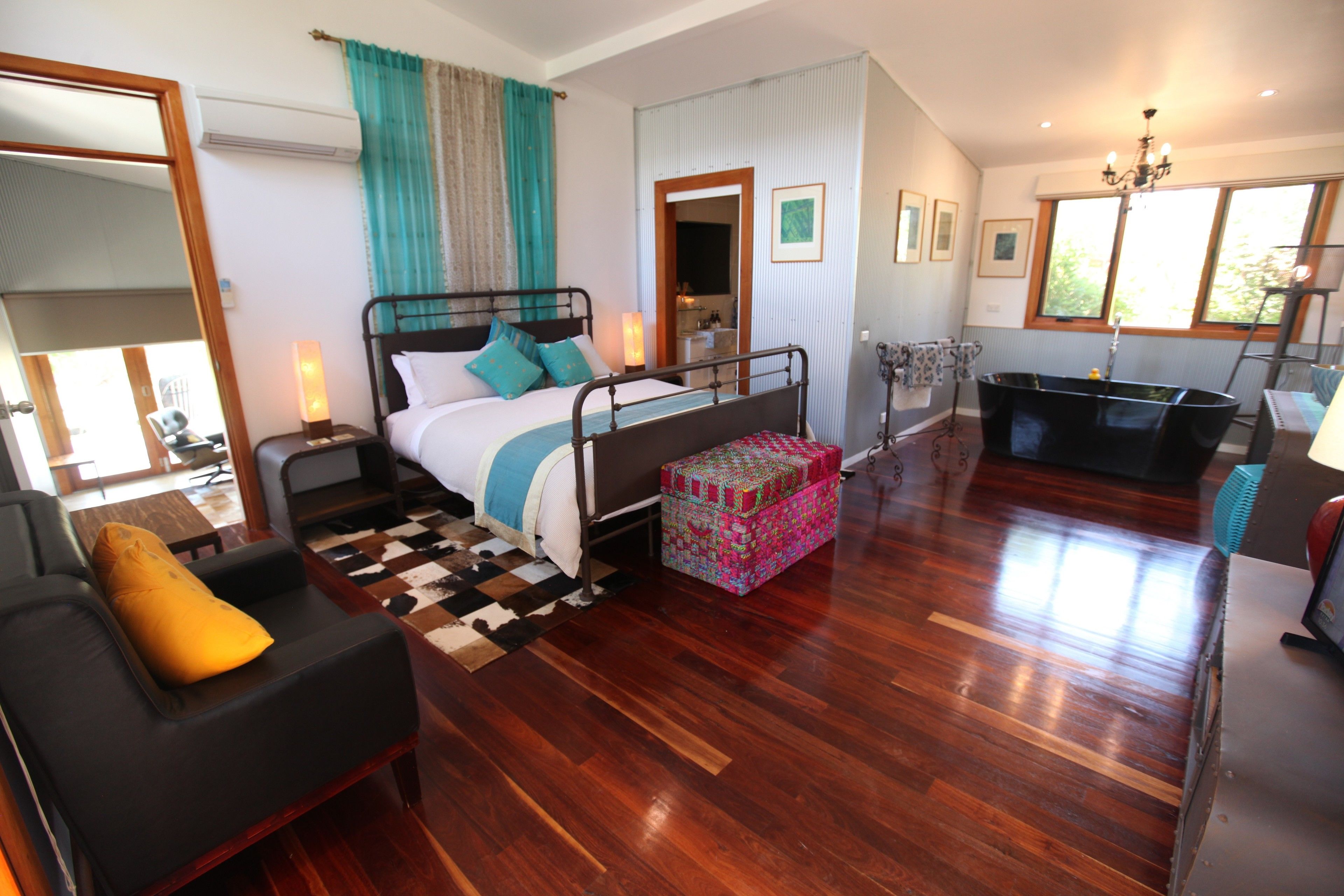 A spacious bedroom with a large bed, a sitting area with a sofa, a chest of drawers, a vanity, and a bathtub.