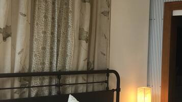 A bed with multiple pillows and a headboard, a bedside lamp, and a curtain with a floral pattern.