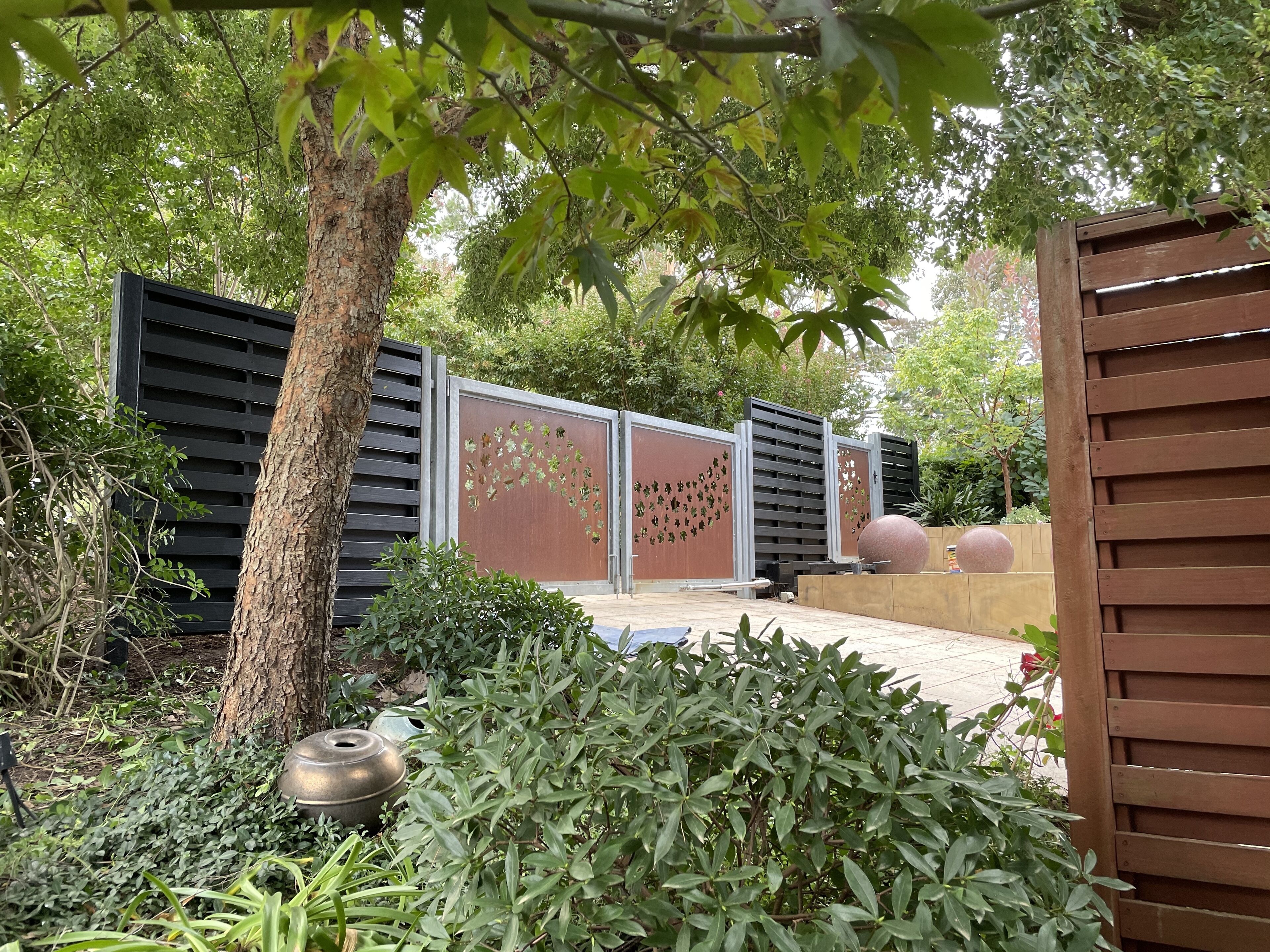 A garden with a metal fence, a tree, and a wooden structure.