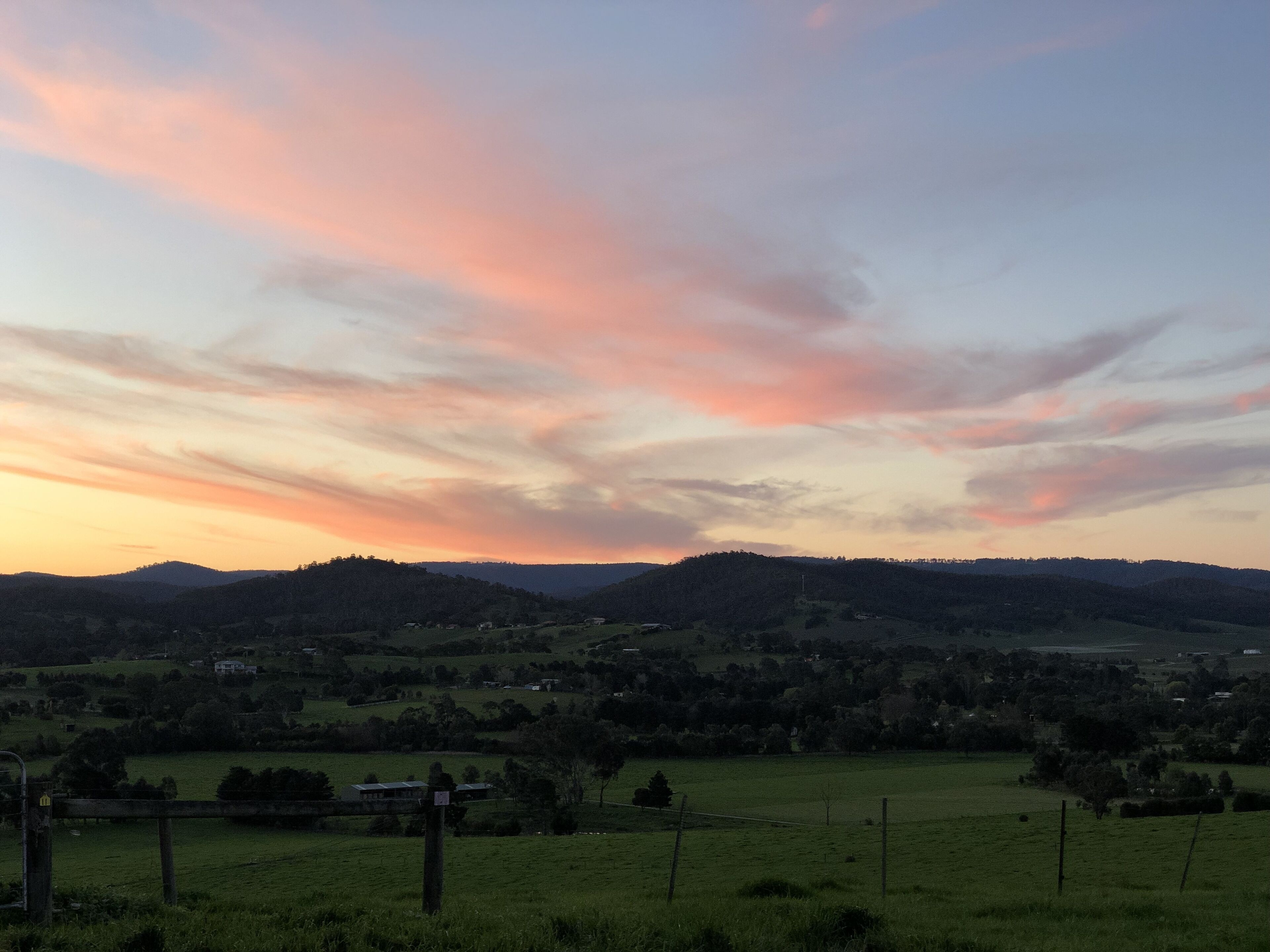 A rural landscape with rolling hills, a fence line, and a few scattered buildings.