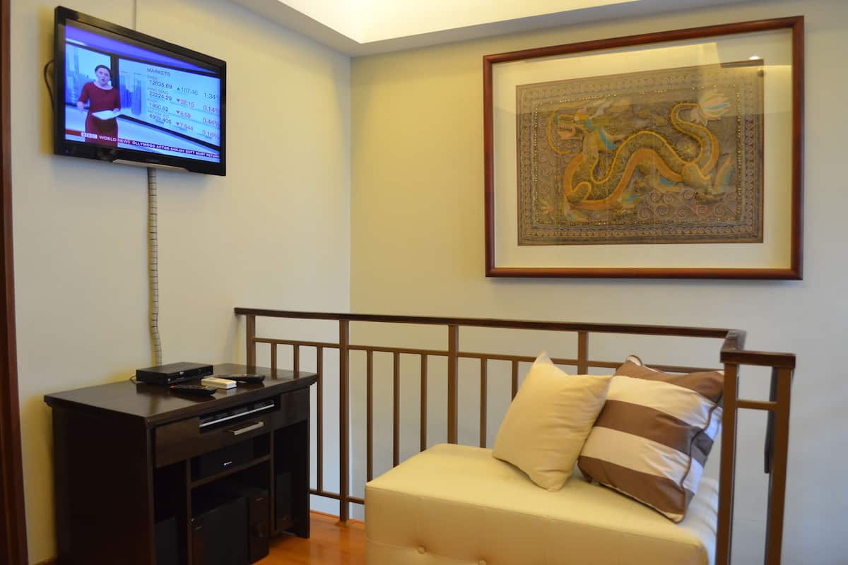 A room with a bed, a TV mounted on the wall, a framed artwork, and a wooden desk with a remote control.