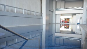 An indoor swimming pool with clear water, a tiled floor, and a view of a room with a red chair and a small table. - Eton Parkview (Makati)
