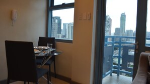 A dining area with a table set for two, a city view through a large window, and a balcony with a railing. - Eton Parkview (Makati)